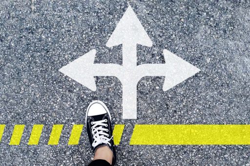 A road, with several arrows painted on the ground, and someone's foot, showing that the person has to choose a path