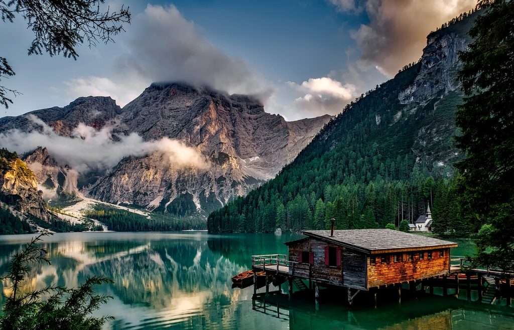 A wooden cabin at the lakeside surrounded by mountains